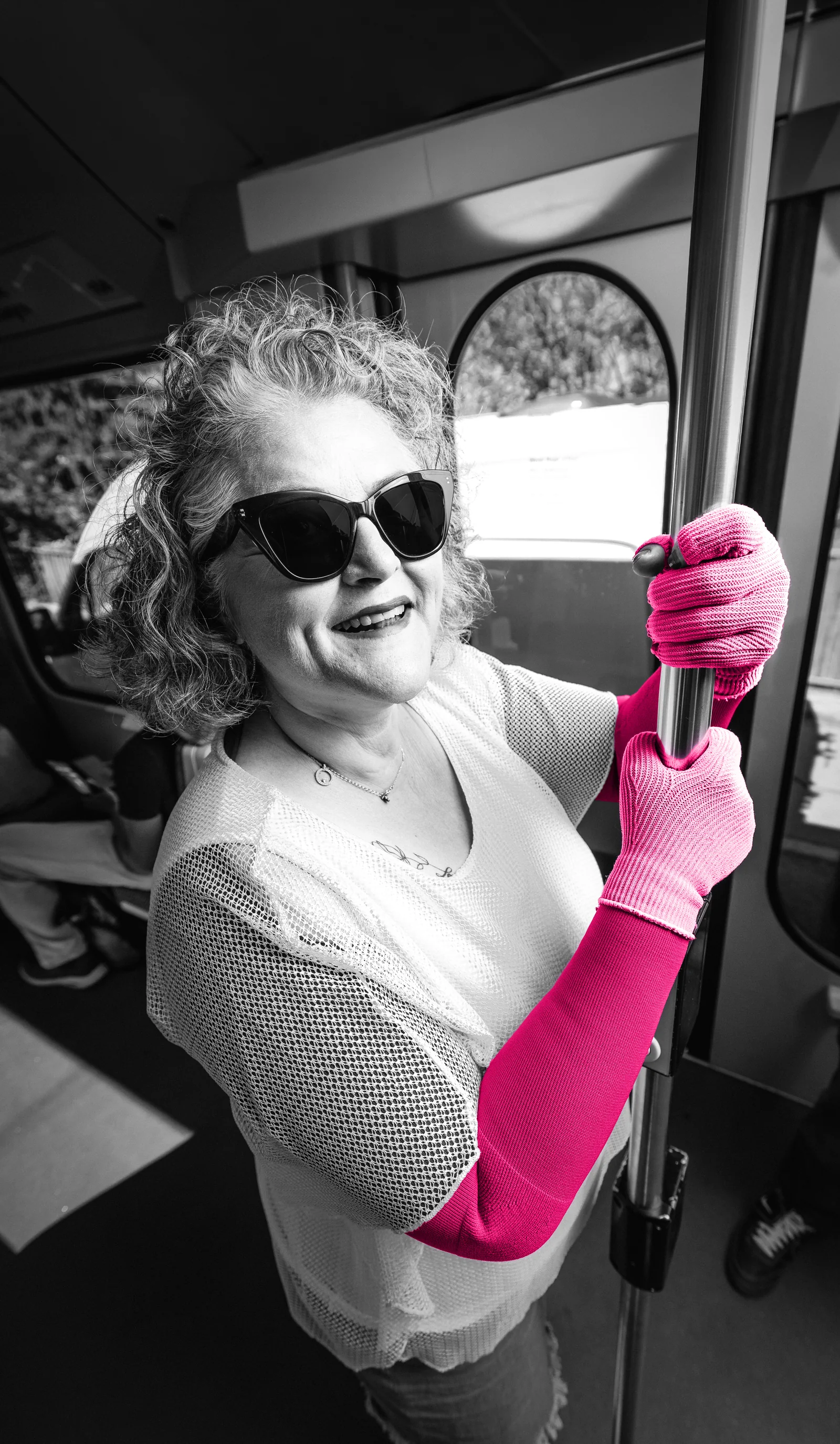 Eine Frau in der Straßenbahn hält sich lachend an der Stange fest, an Arm und Hand pinkfarbene medizinische Kompression.